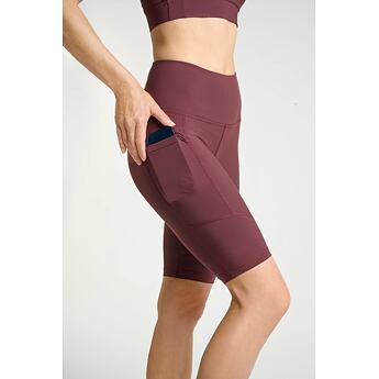 Žena v sportovním setu vkládá mobilní telefon do postranní kapsy dlouhých sportovních kraťasů.